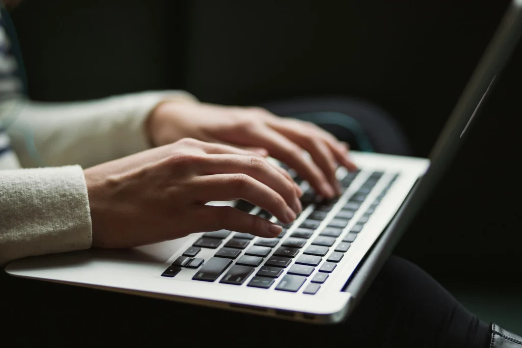 Hands typing on a laptop supporting an article on how to write better ChatGPT prompts.